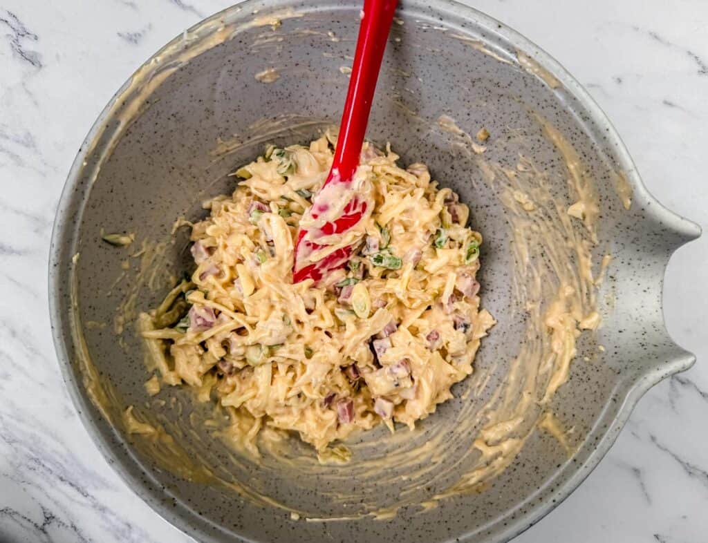 Bowl of mixed ingredients with a red spatula on a marble surface.