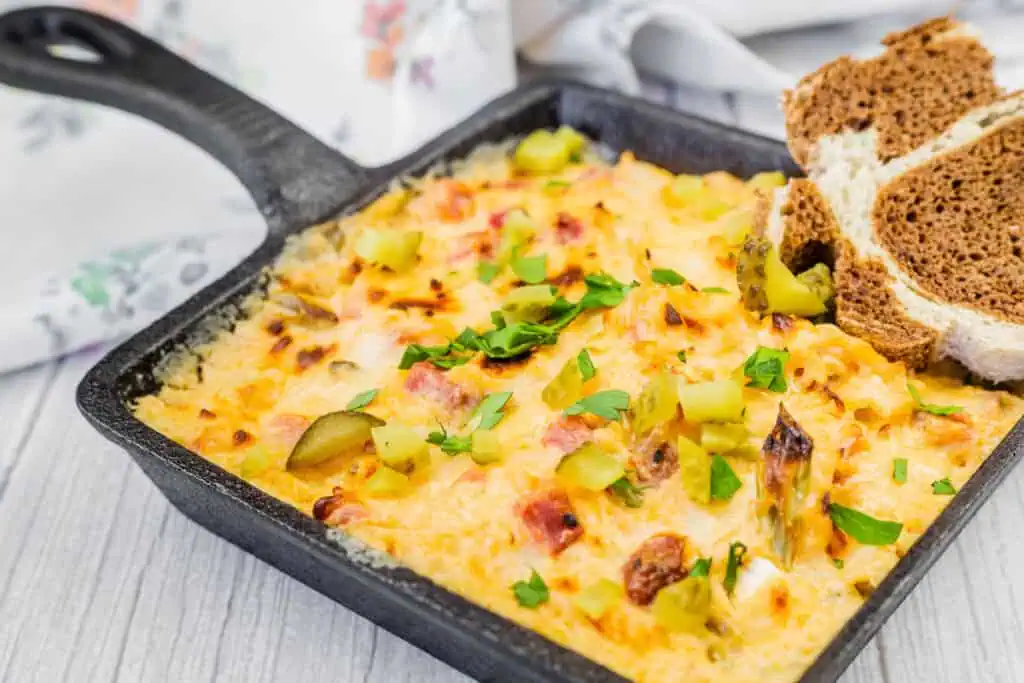 Hot Reuben Dip with chopped dill pickles and herbs in a square skillet served on a slate board with sliced brown bread.