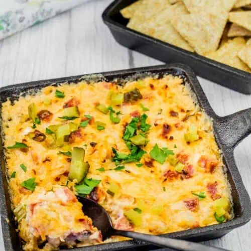 Hot Reuben dip in a cast-iron skillet, garnished with chopped pickles and fresh parsley, served with crispy crackers for dipping.