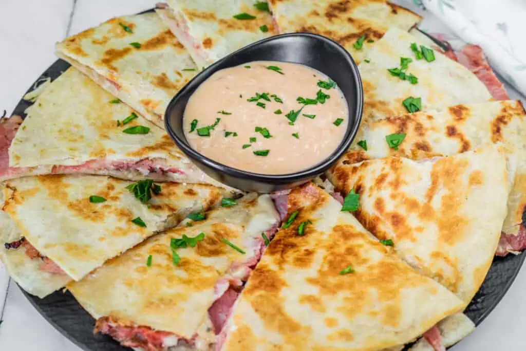 A plate with pieces of Reuben Quesadillas topped with a bowl of sauce.