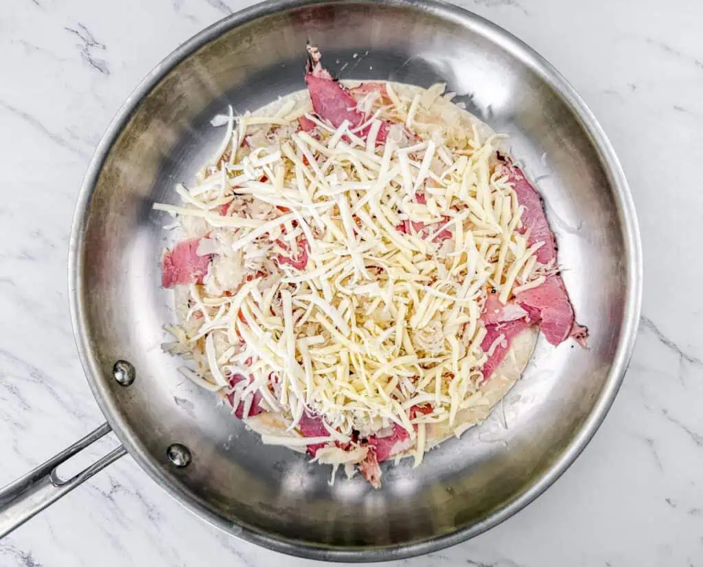 A pan with uncooked cheese, corned beef, and other ingredients on a marble surface.