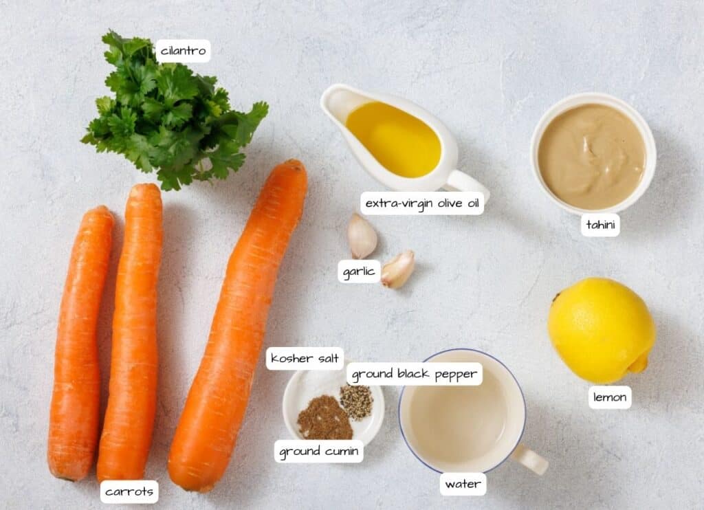 Ingredients on a surface: cilantro, carrots, a lemon, garlic cloves, and bowls of extra-virgin olive oil, tahini, ground cumin, ground black pepper, kosher salt, and water.