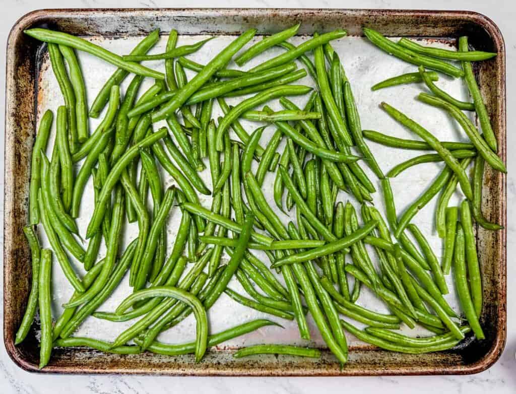 Fresh green beans spread evenly on a metal baking tray.