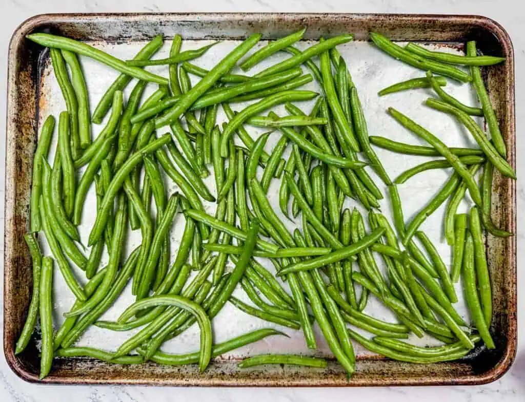 A baking tray filled with raw green beans spread out evenly on a light background.