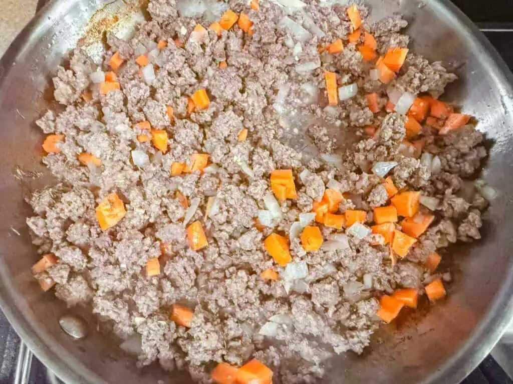 Chopped carrots and onions cooking with ground beef in a frying pan.
