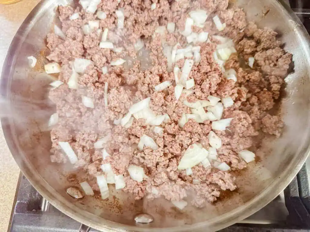 Ground beef and chopped onions cooking in a skillet, with steam rising.