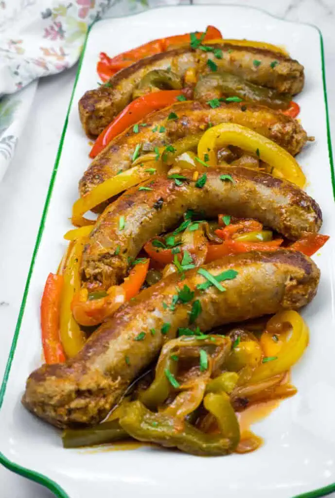 Slow Cooker Sausage & Peppers on a rectangular plate with sliced red, yellow, and green bell peppers, garnished with chopped herbs.