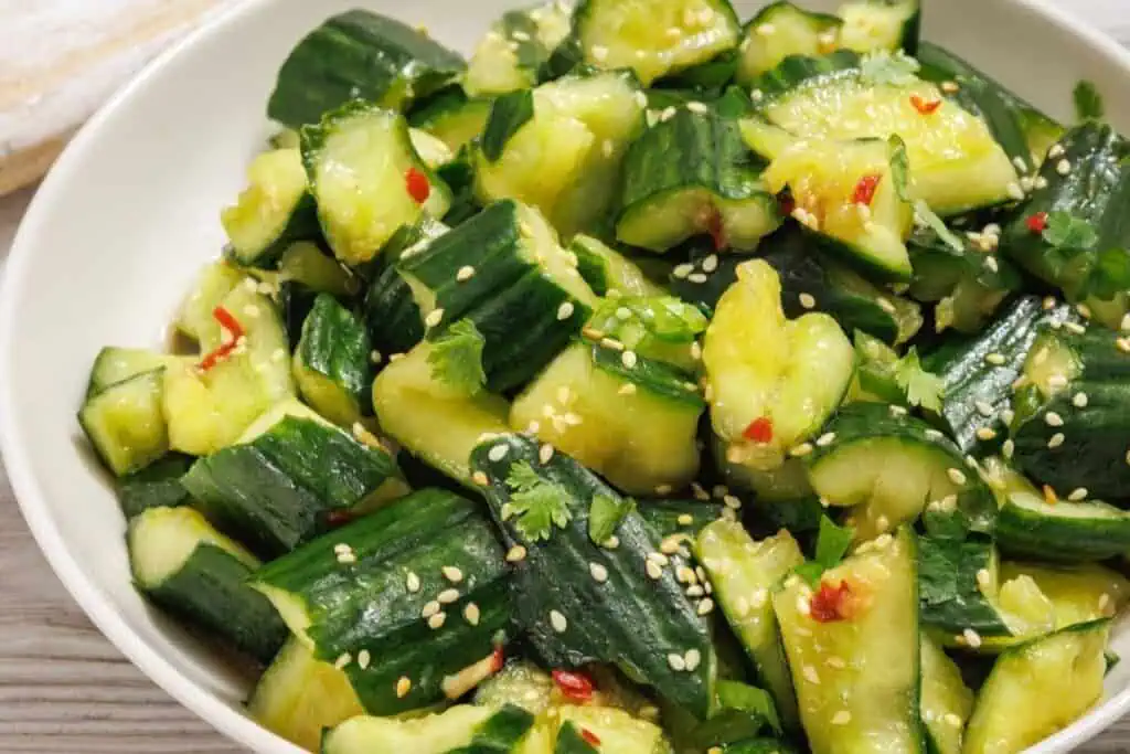 A bowl of smashed cucumber salad garnished with sesame seeds, cilantro, and bits of red chili.