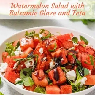 A bowl of watermelon salad with balsamic glaze, feta cheese, and greens, set against a light background. The text reads "Watermelon Salad with Balsamic Glaze and Feta.