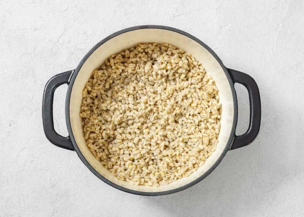 A black pot filled with cooked pearl barley sits on a light gray surface.