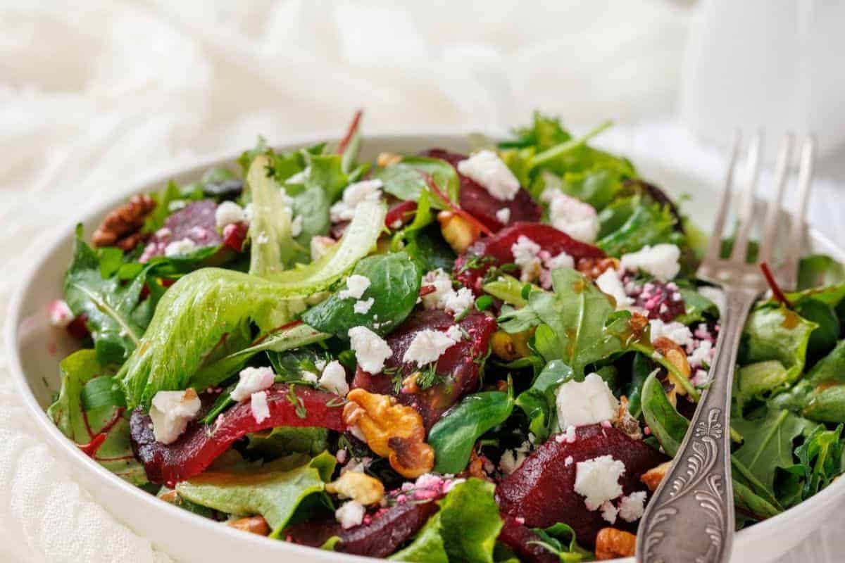 A Beet Salad with Goat Cheese and Walnuts in a white bowl, accompanied by a fork.