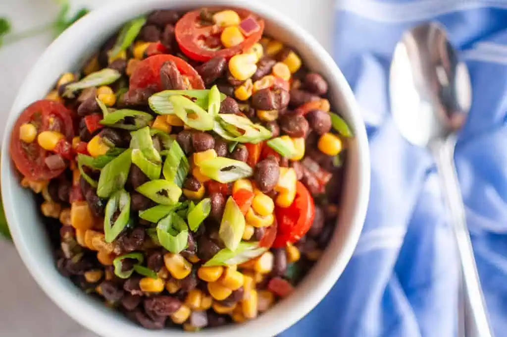 A bowl of black bean and corn salad placed next to a spoon and a blue napkin.