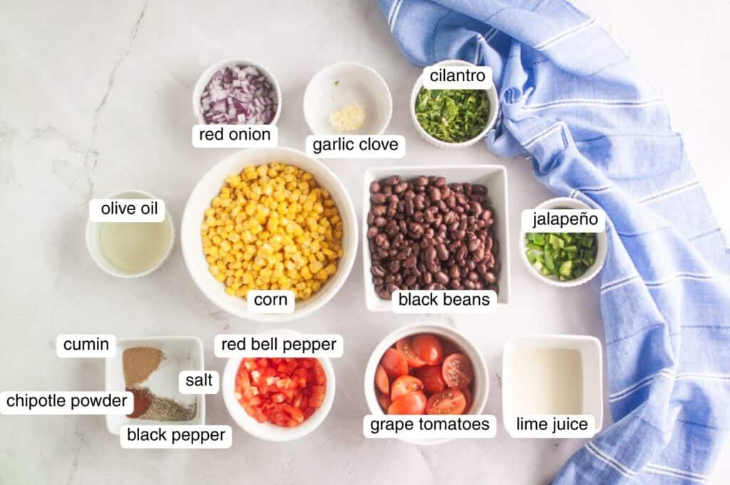 Ingredients for a black bean and corn salad arranged in bowls, including corn, black beans, tomatoes, red onion, red bell pepper, jalape&ntilde;o, cilantro, garlic, spices, olive oil, and lime juice.