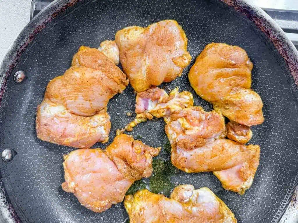 Raw, seasoned chicken pieces are arranged in a frying pan, ready to be cooked.