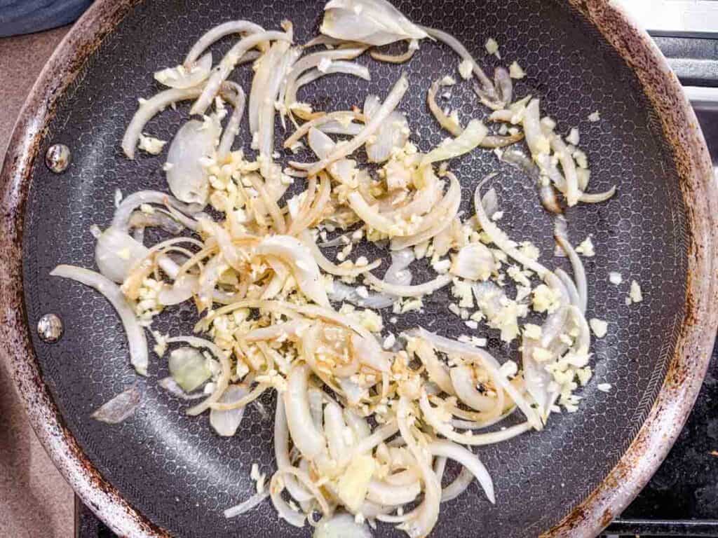 Sliced onions and minced garlic cooking in a frying pan.