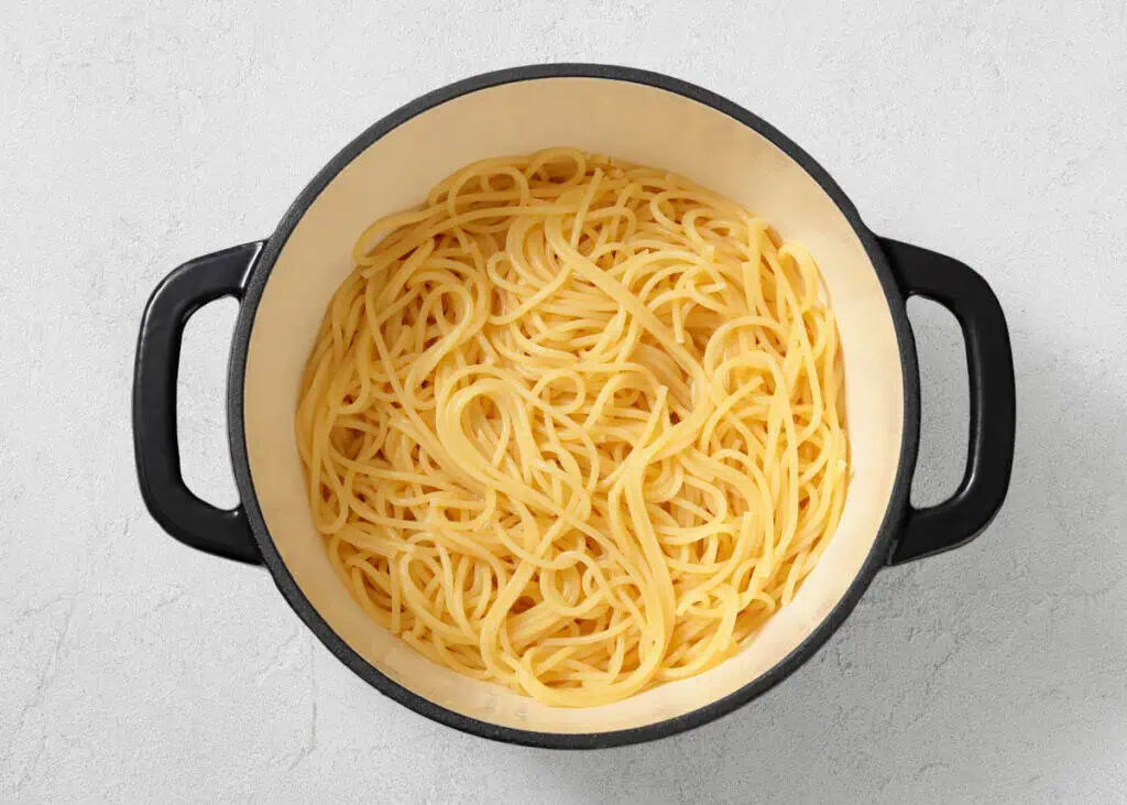 A large black pot filled with plain cooked spaghetti noodles sits on a light-colored surface.