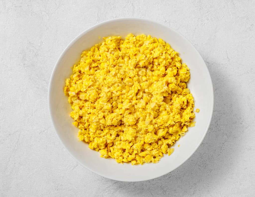 A white bowl filled with corn mixture sits on a light gray surface.