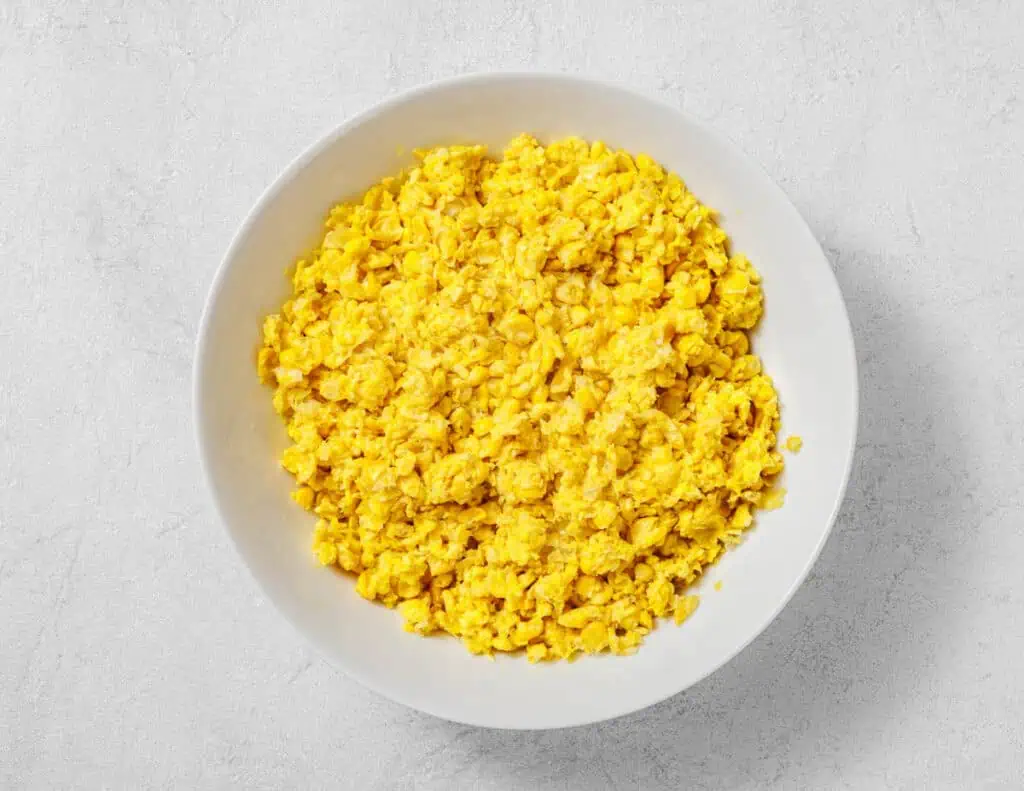 A white bowl filled with corn mixture sits on a light gray surface.