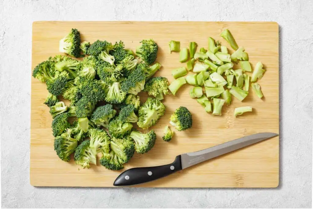 Chopped broccoli florets and stems on a wooden cutting board with a black-handled knife.