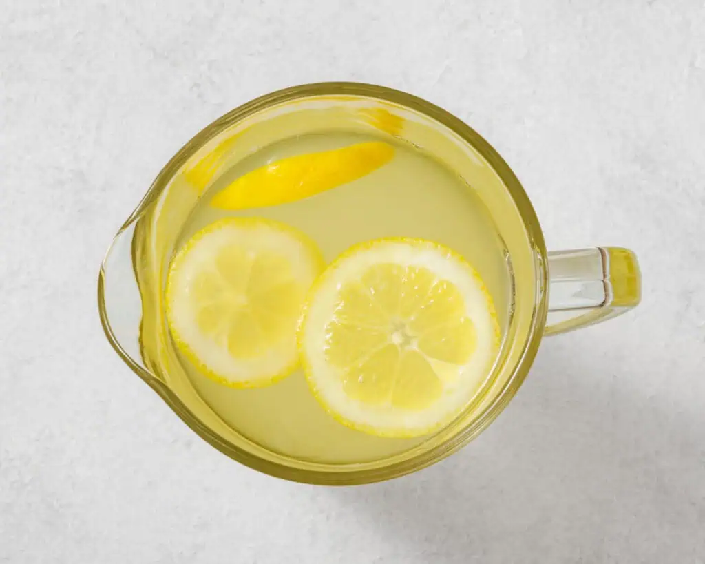 Top-down view of a clear pitcher with lemonade and lemon slices on a light gray surface.
