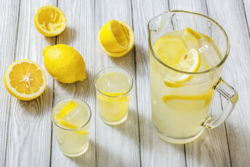 Lemonade in a pitcher and glasses with lemons on a wooden surface.