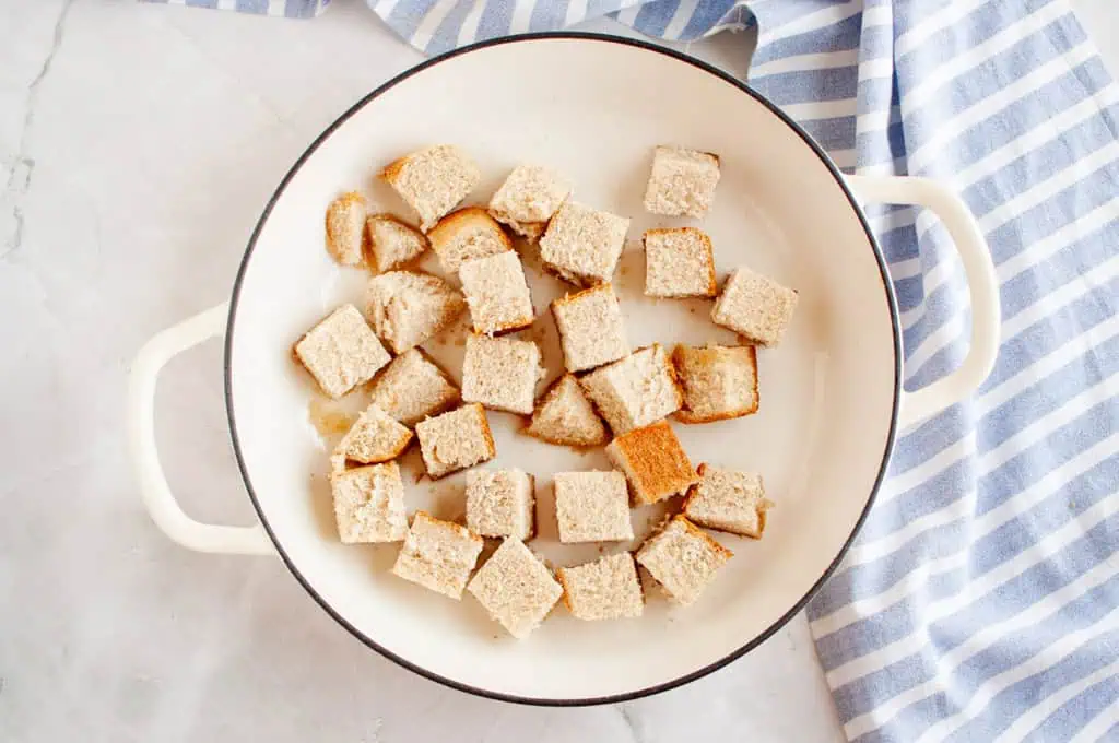 Overhead shot of bread cubes in a white pan, with a striped cloth.