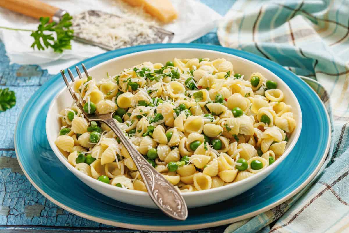 A bowl of pasta and peas with a fork, grater, and cheese on the side.