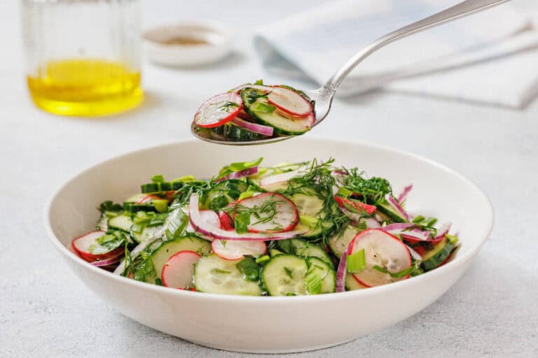 A spoonful of Radish Salad is held above a white bowl filled with the same salad.
