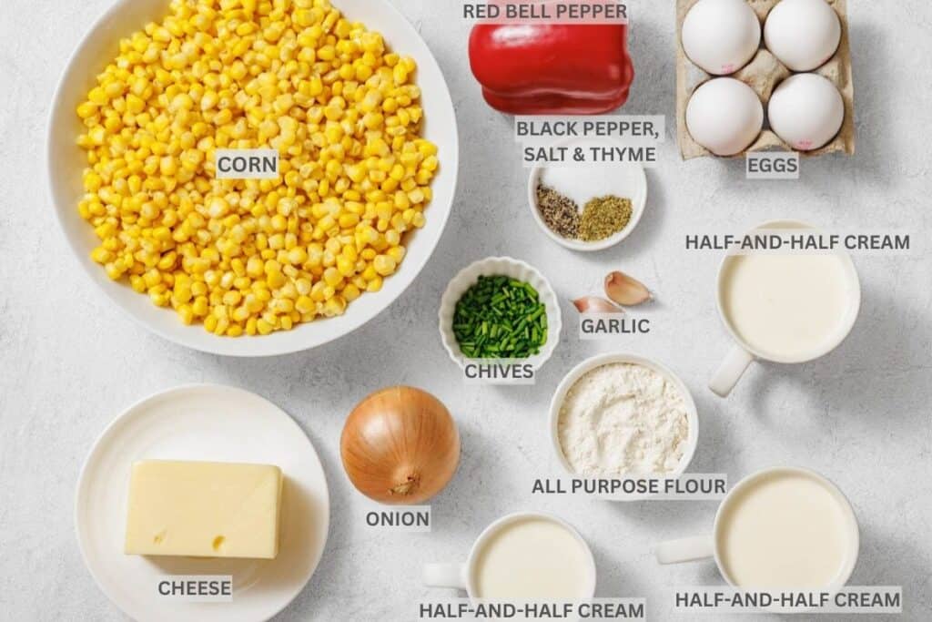 Assorted labeled ingredients for a recipe, including corn, red bell pepper, eggs, cheese, onion, chives, garlic, flour, half-and-half cream, and seasonings arranged on a white surface.
