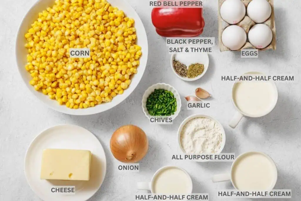 Assorted labeled ingredients for a recipe, including corn, red bell pepper, eggs, cheese, onion, chives, garlic, flour, half-and-half cream, and seasonings arranged on a white surface.