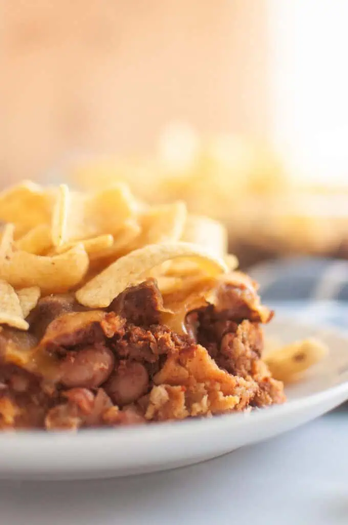 A close up take of Frito Pie in a small white plate on a white table with corn chips on top.