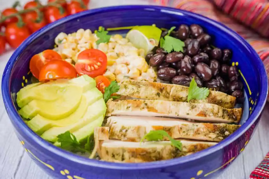 A blue bowl filled with southwest chicken salad, featuring grilled chicken, corn, tomatoes, avocado, and black beans.