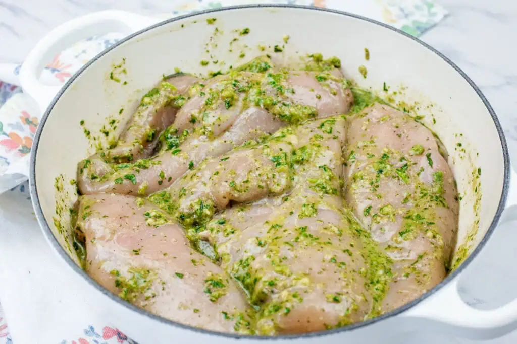Raw chicken breasts coated with herbs seasonings in a white bowl.
