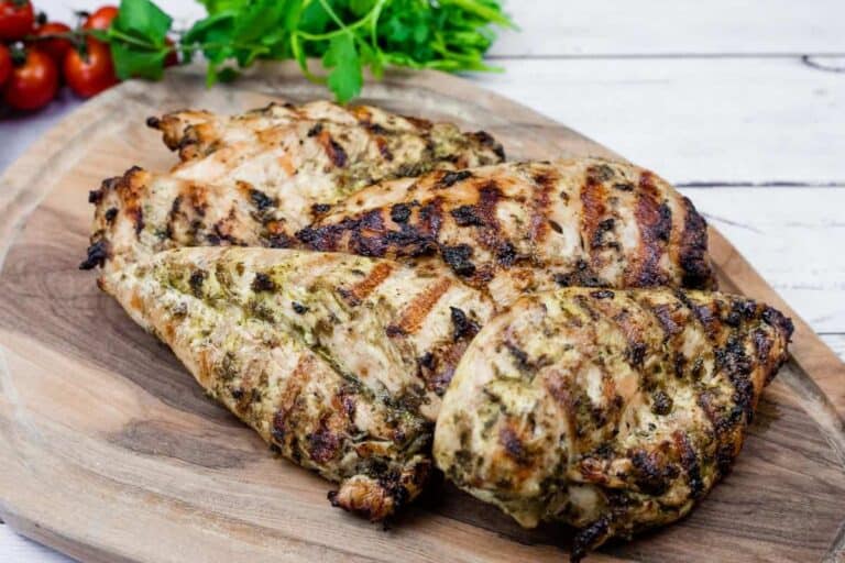 Grilled chicken on a wooden board with cilantro and tomatoes in the back.
