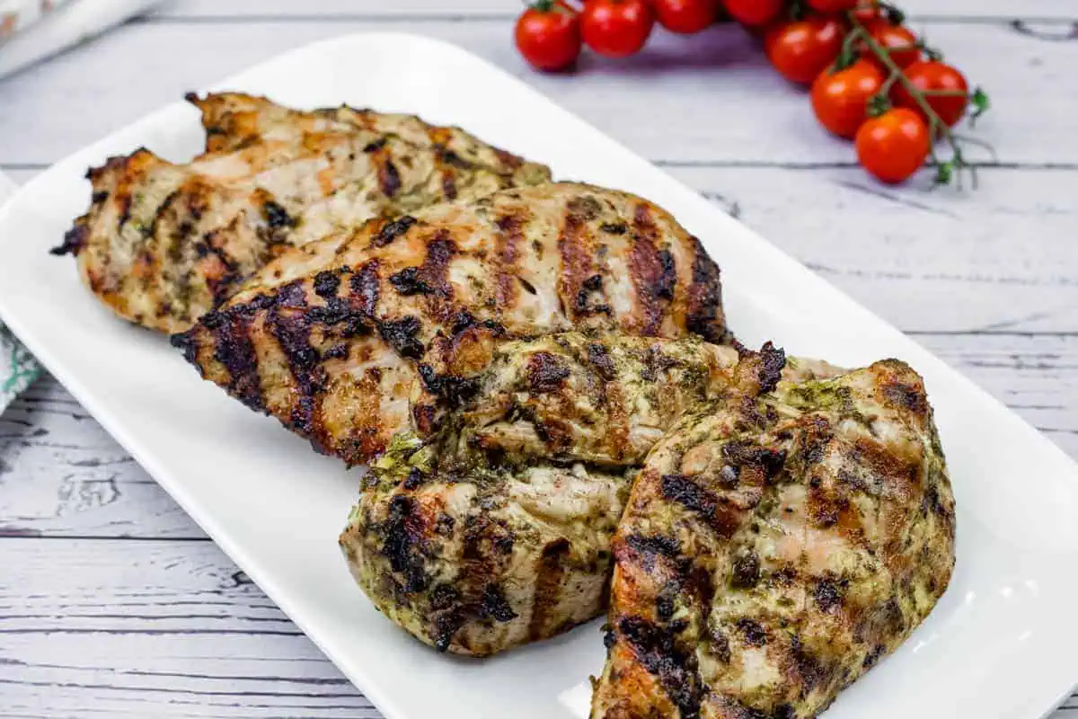 Grilled lime-garlic chicken breasts with visible char marks on a white rectangular plate, with vine tomatoes in the background.