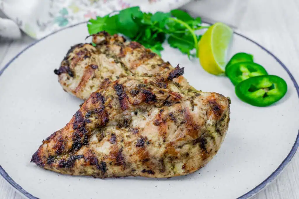 Grilled Lime Garlic Chicken on a white plate with cilantro and a slice of lemon on the side.