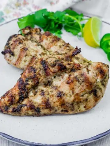 Grilled chicken with cilantro leaves and a slice of lemon in a white plate.