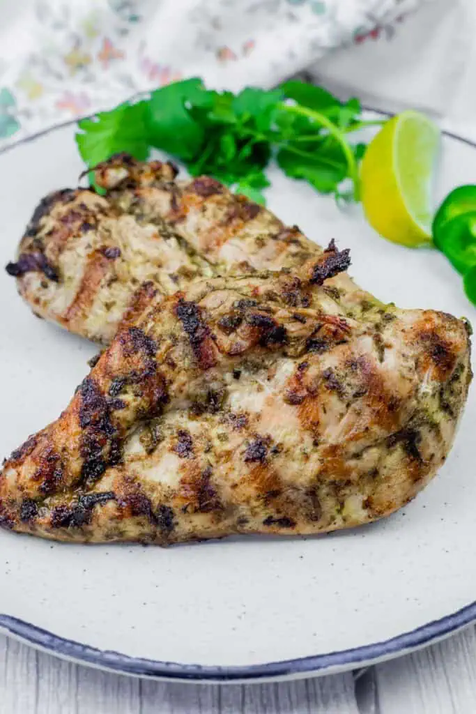 Grilled chicken with cilantro leaves and a slice of lemon in a white plate.