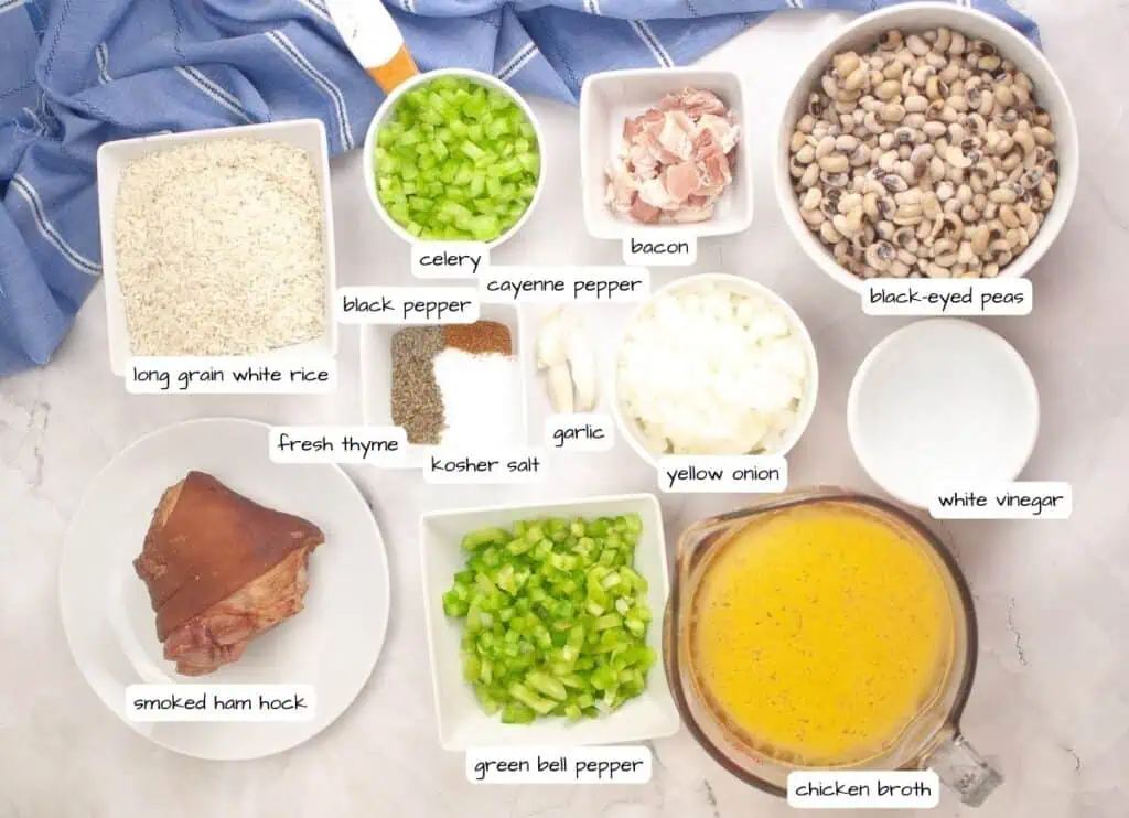 Overhead view of labeled ingredients for a dish, including rice, celery, bacon, black-eyed peas, spices, onion, vinegar, ham hock, bell pepper, garlic, and chicken broth.