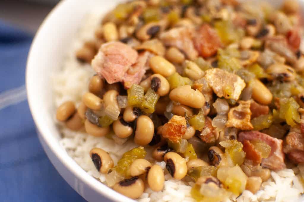 A close-up of a bowl filled with cooked white rice topped with black-eyed peas, diced vegetables, and pieces of meat.