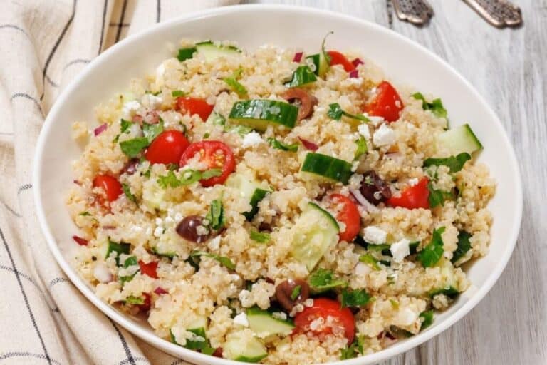 A bowl of Easy Mediterranean Quinoa Salad on a wooden surface with a striped cloth nearby.