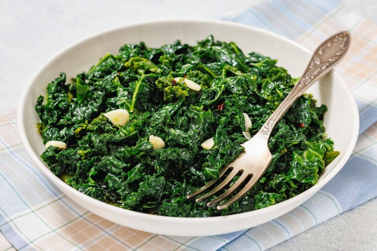 A white bowl filled with Simple Saut&eacute;ed Kale, with a fork resting on the side.