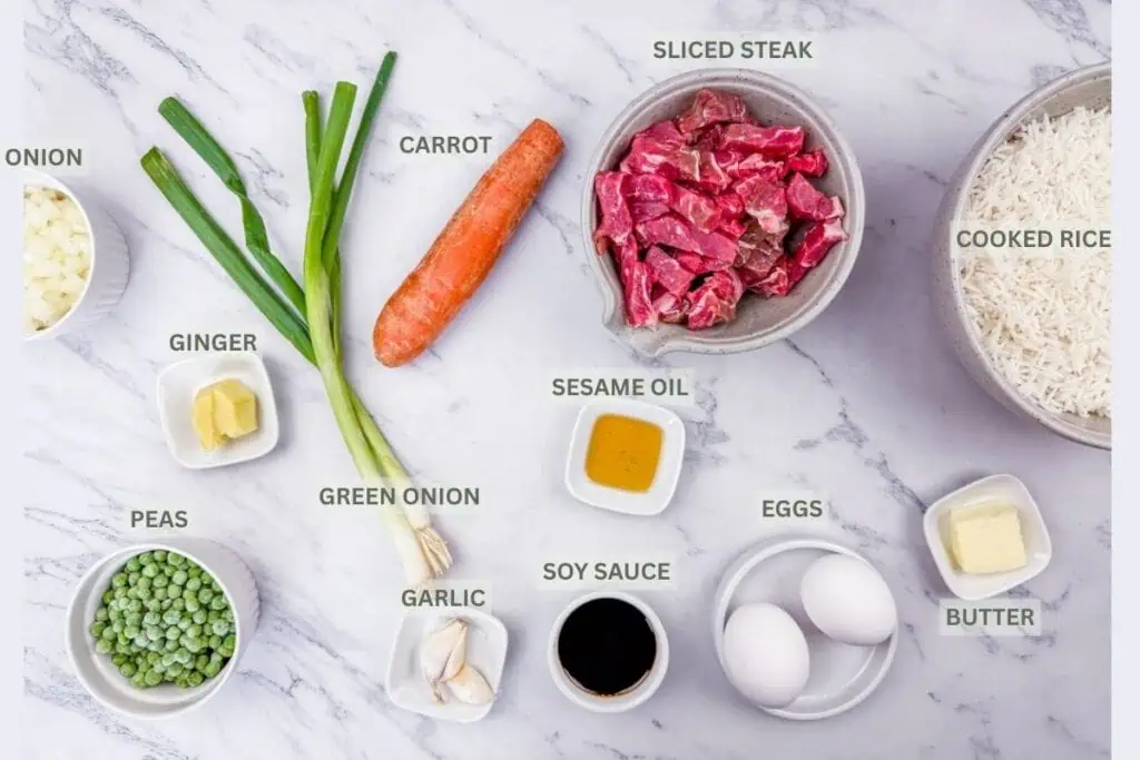 Rice, sliced steak, carrot, oil, eggs, butter, soy sauce, garlic, peeled ginger, sliced onion, green onion, and peas on a marbled white-gray surface with labels