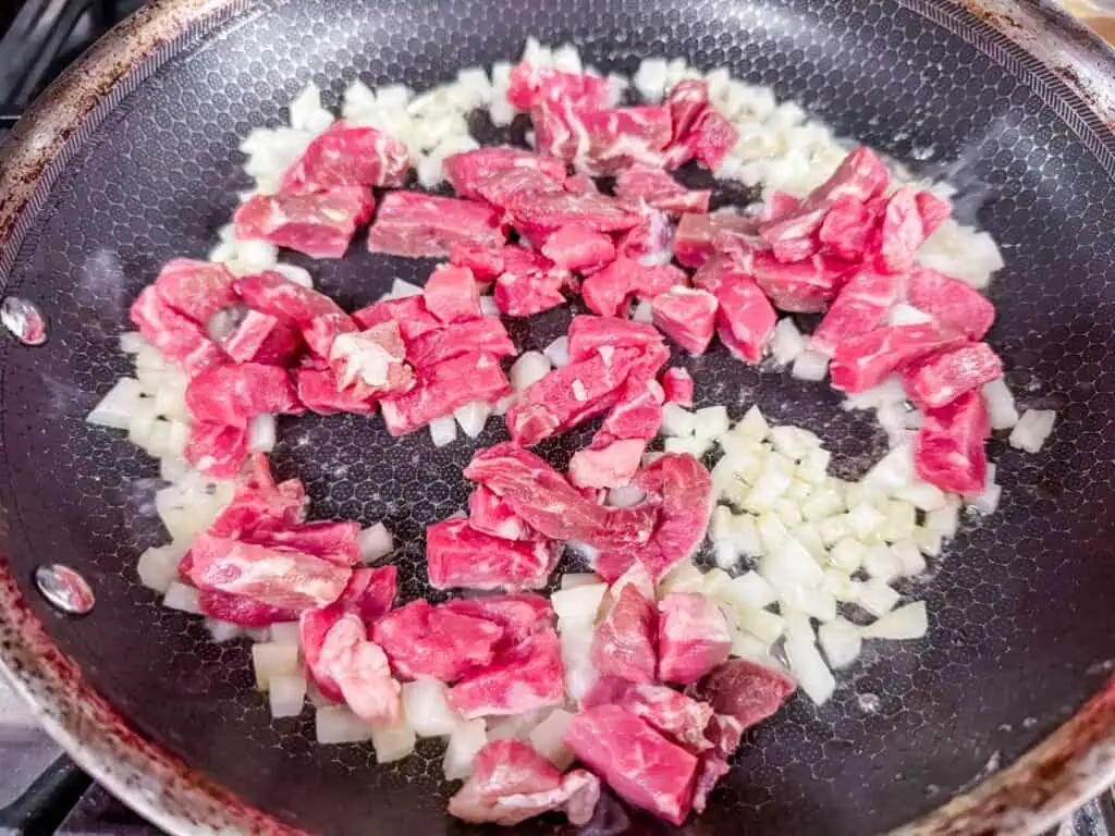 seared onions with raw diced steak in a skillet.
