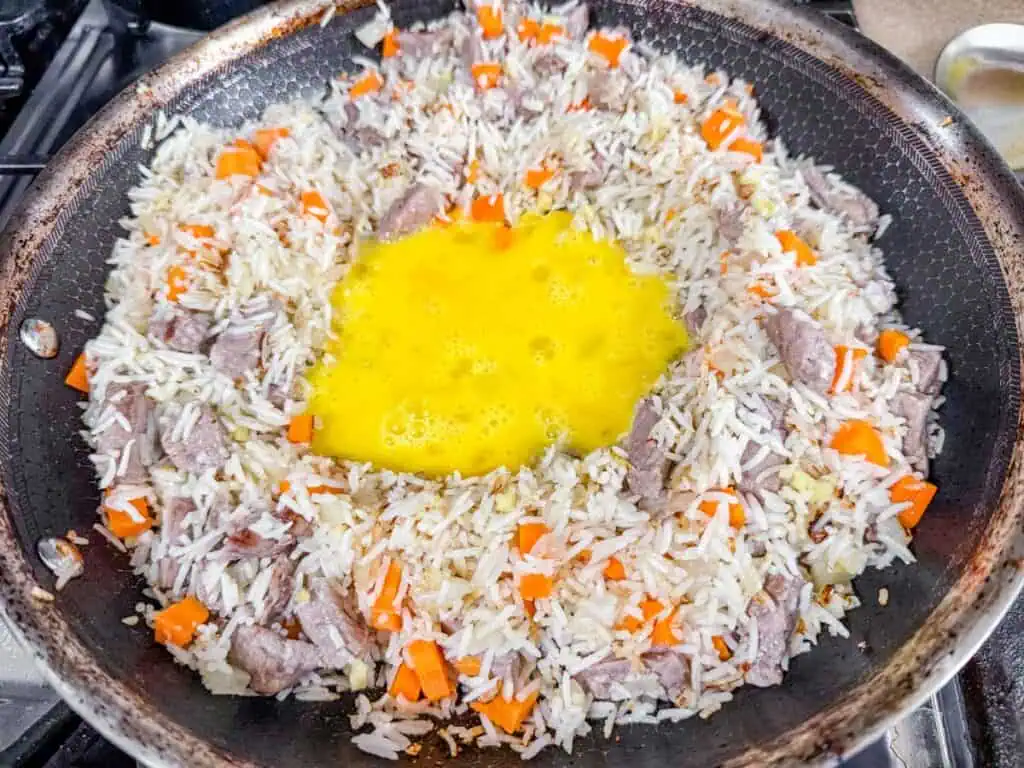 seared rice with carrots and raw egg in the middle of a skillet pan.