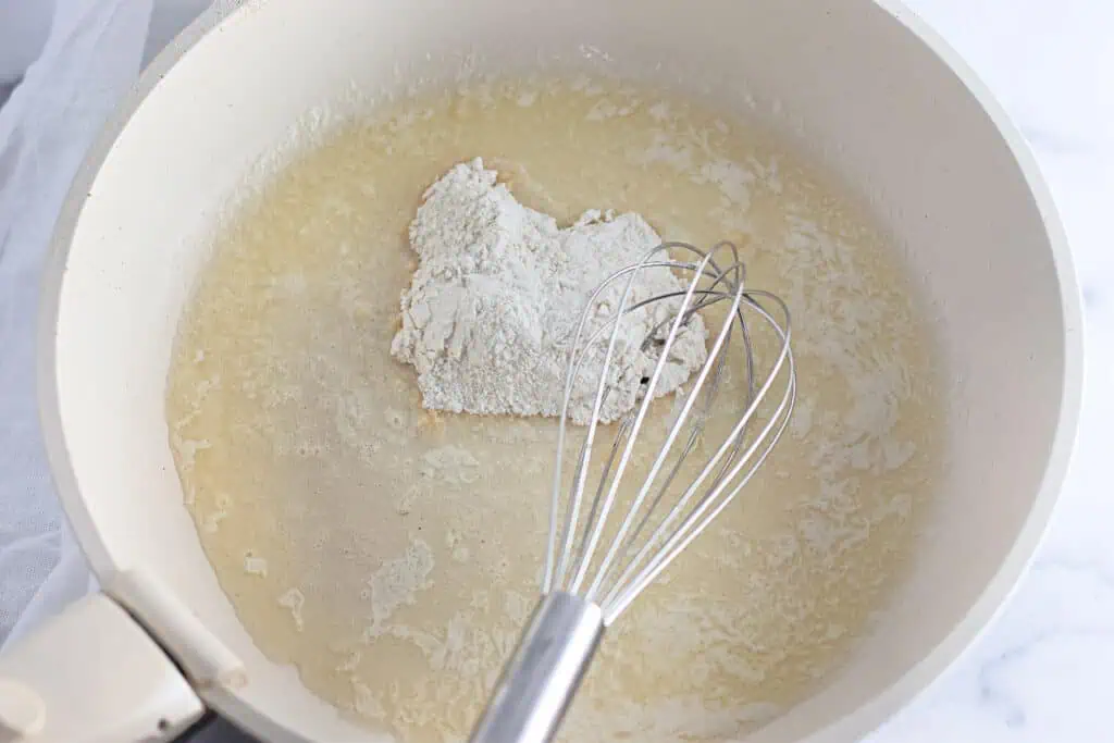 A whisk in a light-colored pan stirring flour into melted butter to make a roux.