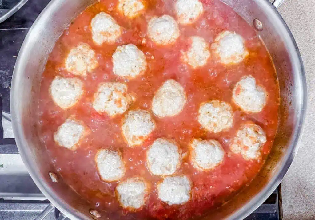 A pan of meatballs simmering in tomato sauce on a stovetop.