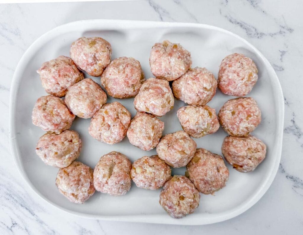 A white tray with raw meatballs arranged in rows on a marble surface.