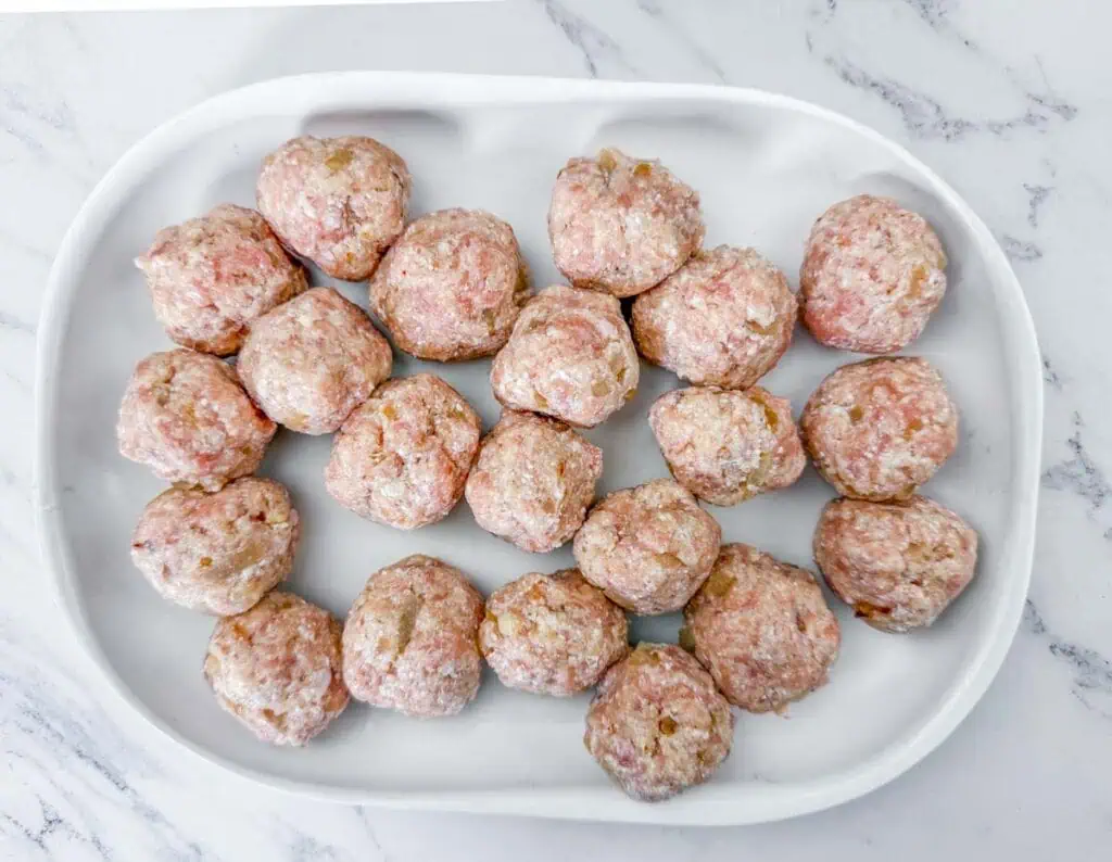 A white tray with raw meatballs arranged in rows on a marble surface.