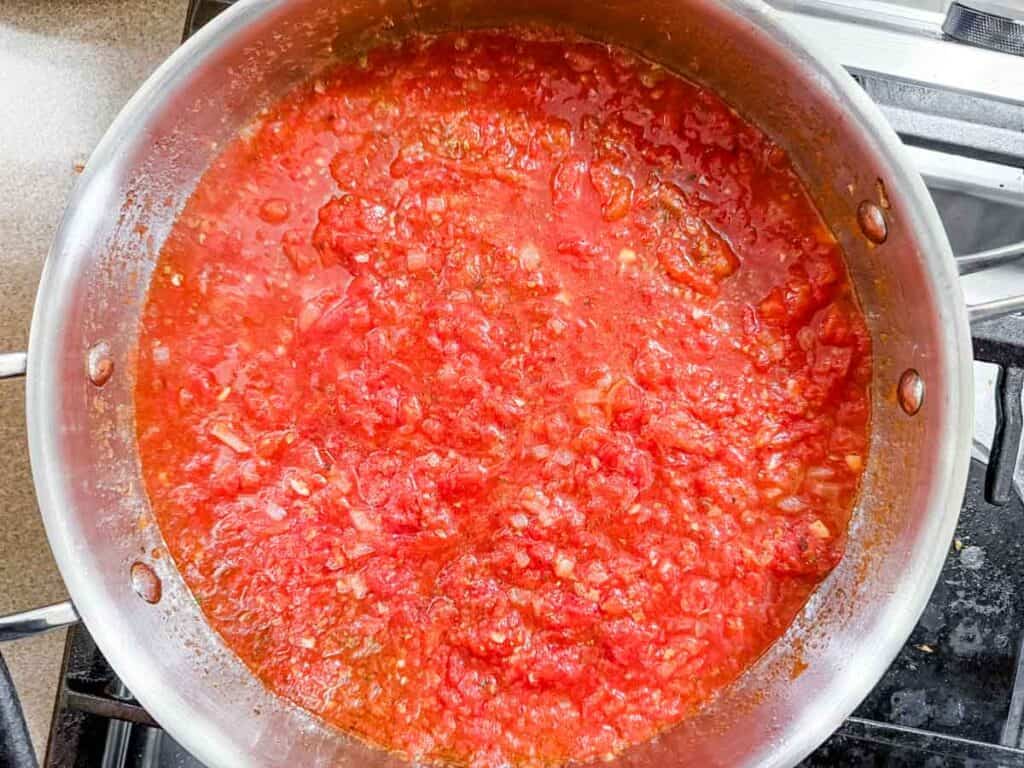 A stainless steel pan filled with simmering tomato sauce on a stovetop.